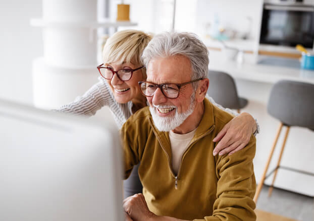 Senior couple smiling while looking at their desktop computer