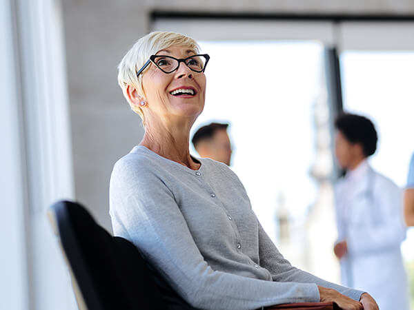 Gray-haired woman with glasses smiling while waiting in an urgent care's lobby