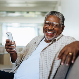 Black senior male smiling while holding his smartphone