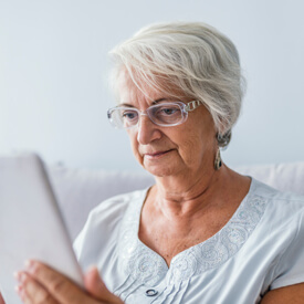 Gray-haired woman in glasses looking at her tablet device