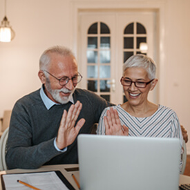 Senior couple smiling and waving at their laptop screen